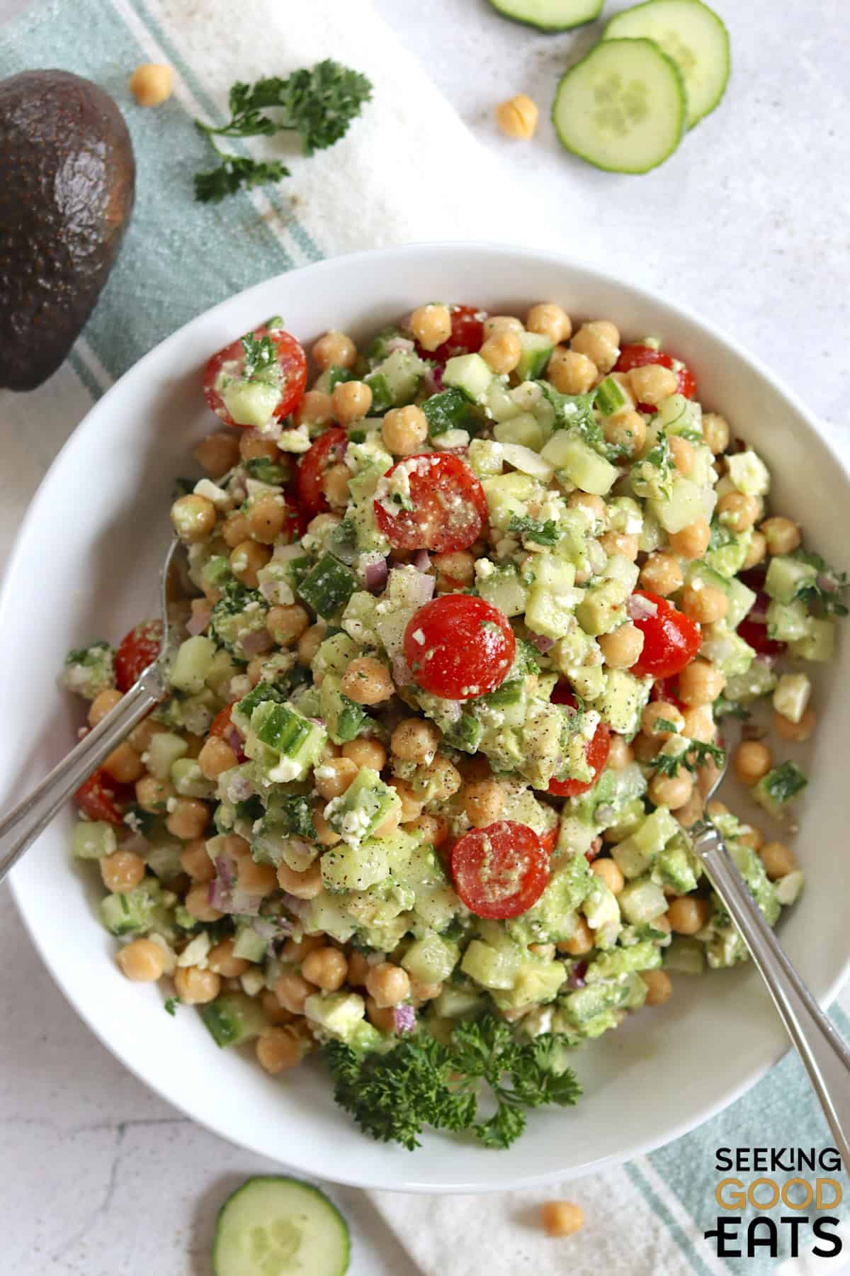 A white serving bowl filled with feta avocado chickpea salad and two serving spoons.