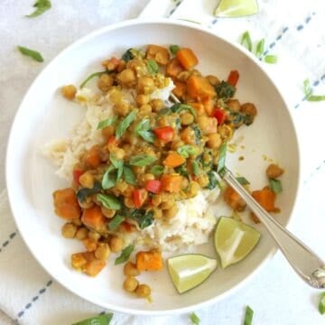 Chickpea coconut curry in a white bowl over rice with lime wedges and green onion.