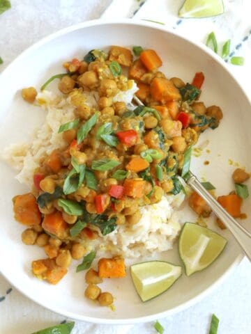 Chickpea coconut curry in a white bowl over rice with lime wedges and green onion.