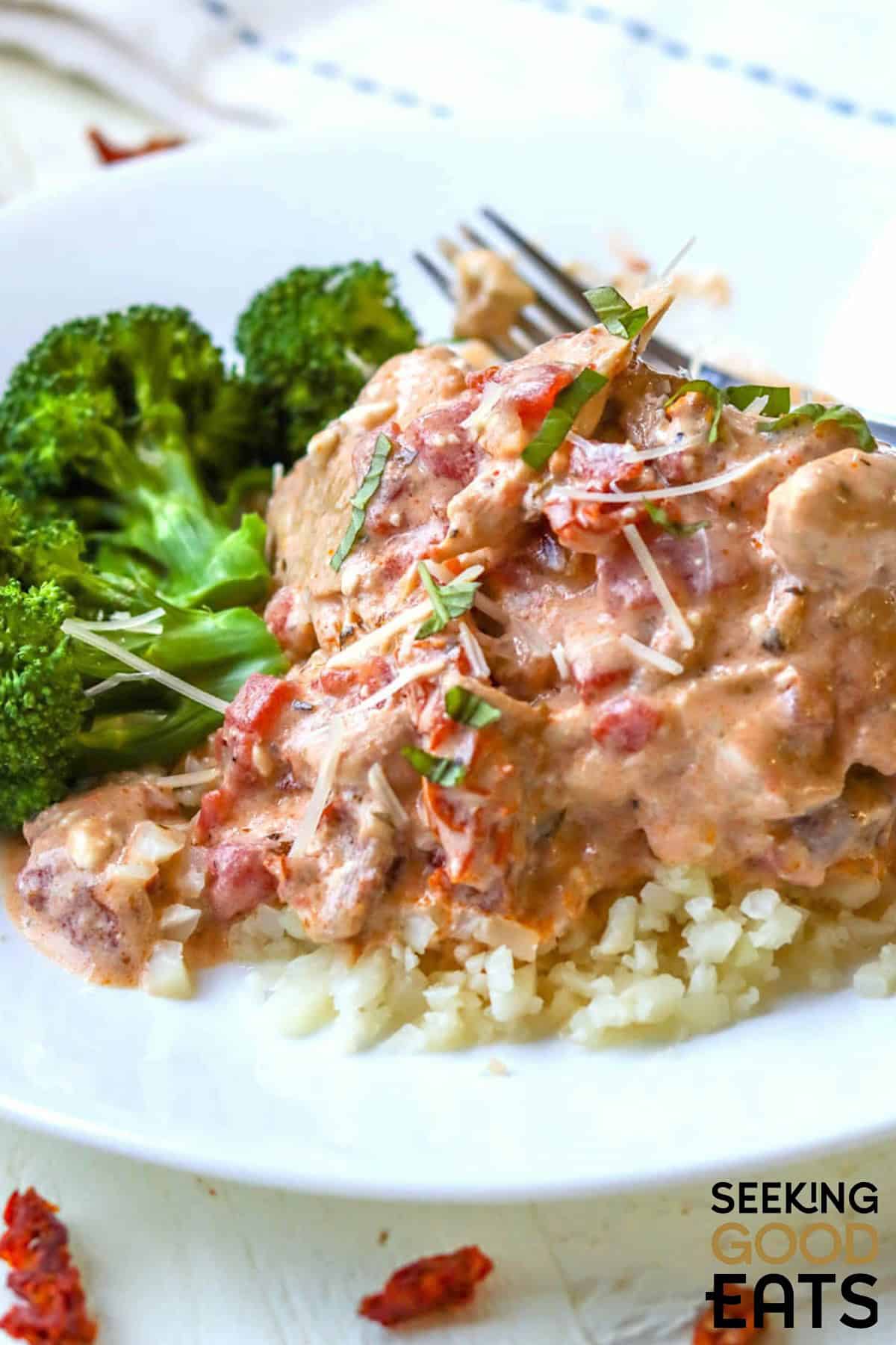 Italian crockpot chicken thighs in tomato basil cream sauce over riced cauliflower on a white plate.