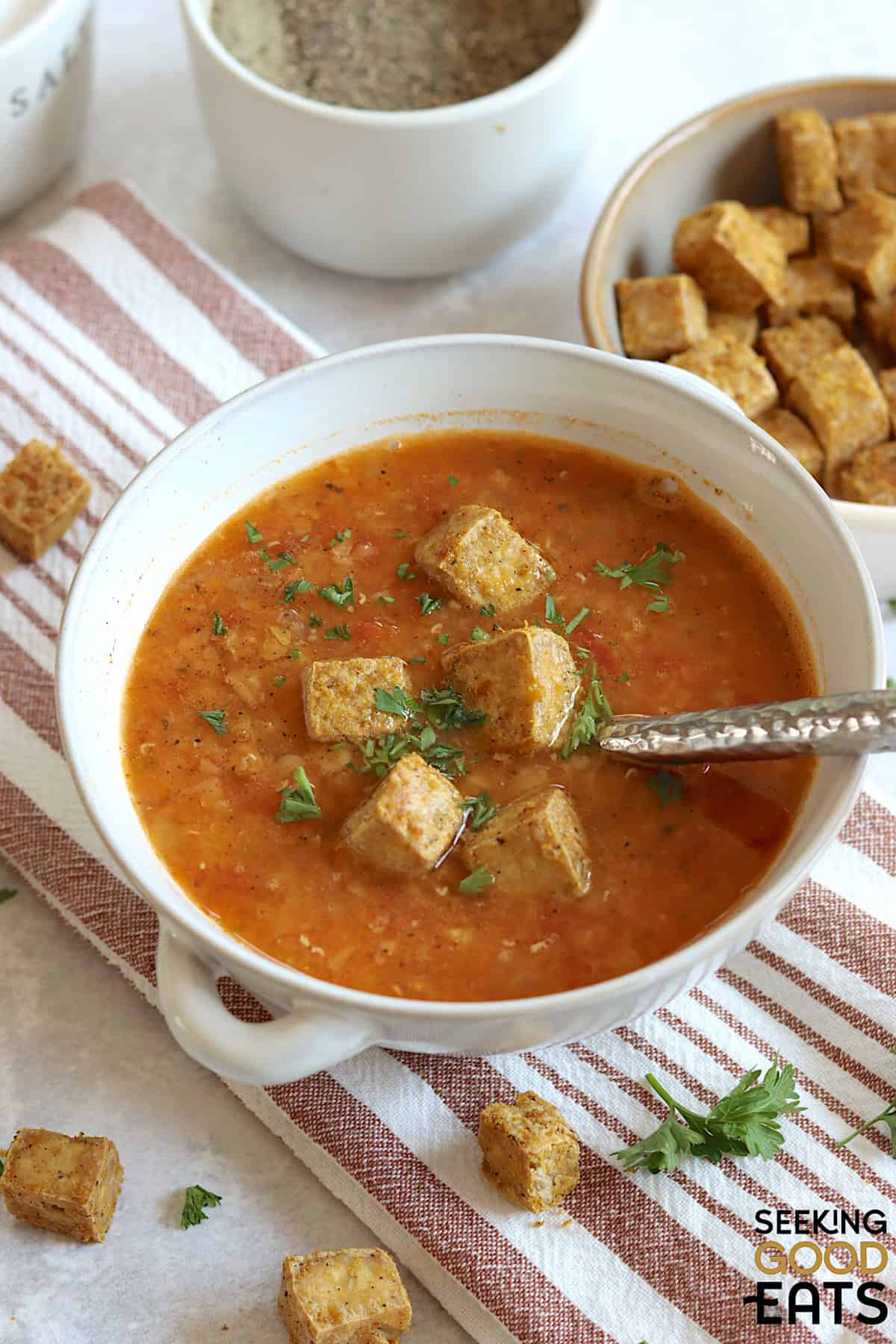A white bowl of red lentil tomato soup vegan recipe with tofu croutons and fresh parsley.