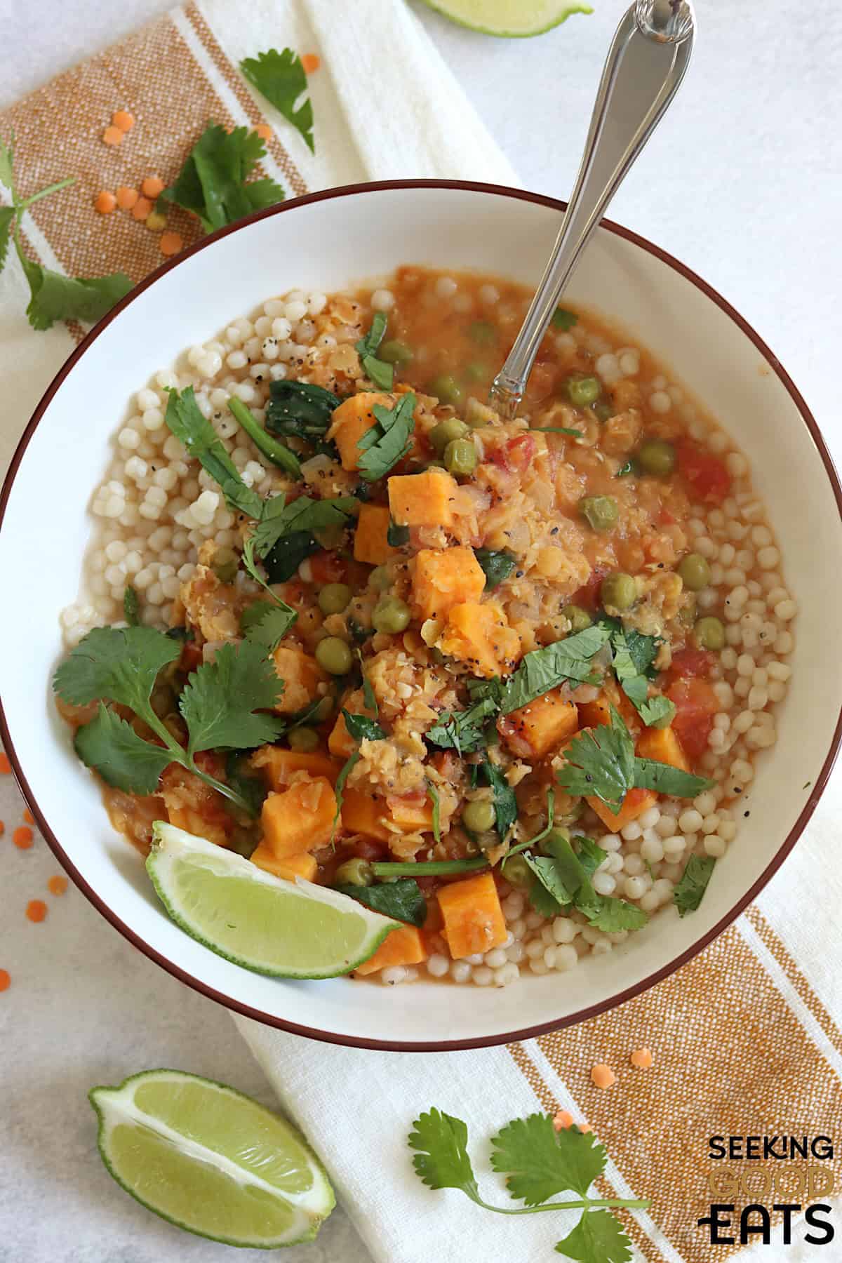 A white bowl filled with sweet potato red lentil curry recipe and silver spoon.
