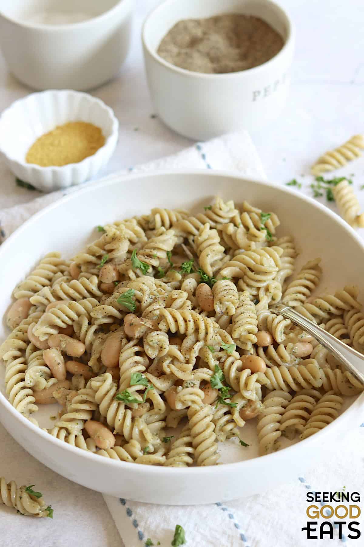Pesto pasta vegan recipe with white beans and fresh parsley in a white bowl.
