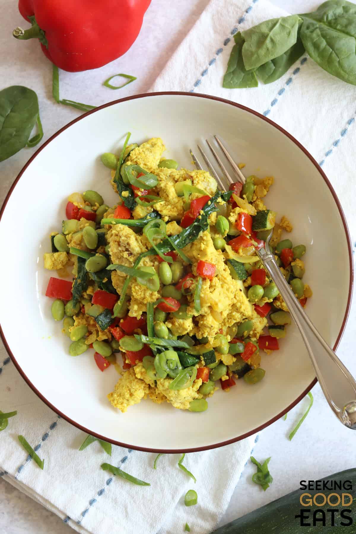 Tofu scramble in a white bowl with green edamame and red bell pepper.