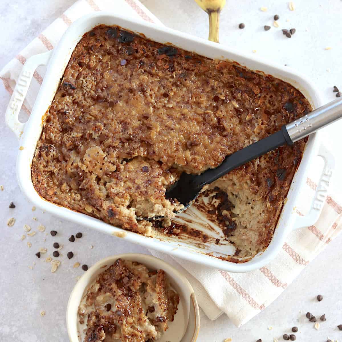 Banana chocolate chip baked oatmeal in a rectangle white pan and black serving spoon.