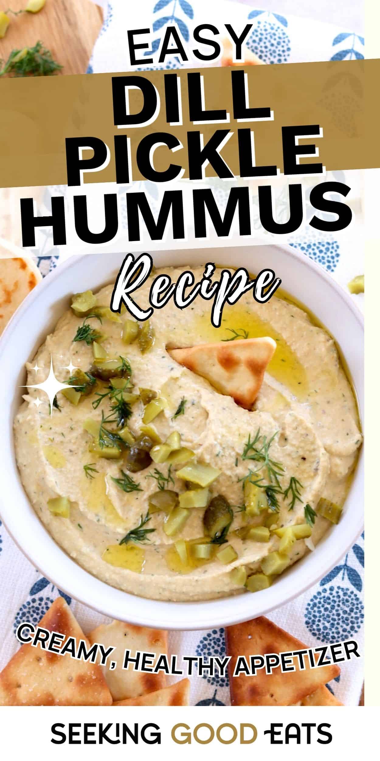 A bowl of dill pickle hummus topped with chopped pickles, dill, and olive oil, served with pita chips. Creamy hummus flavored with dill pickles.