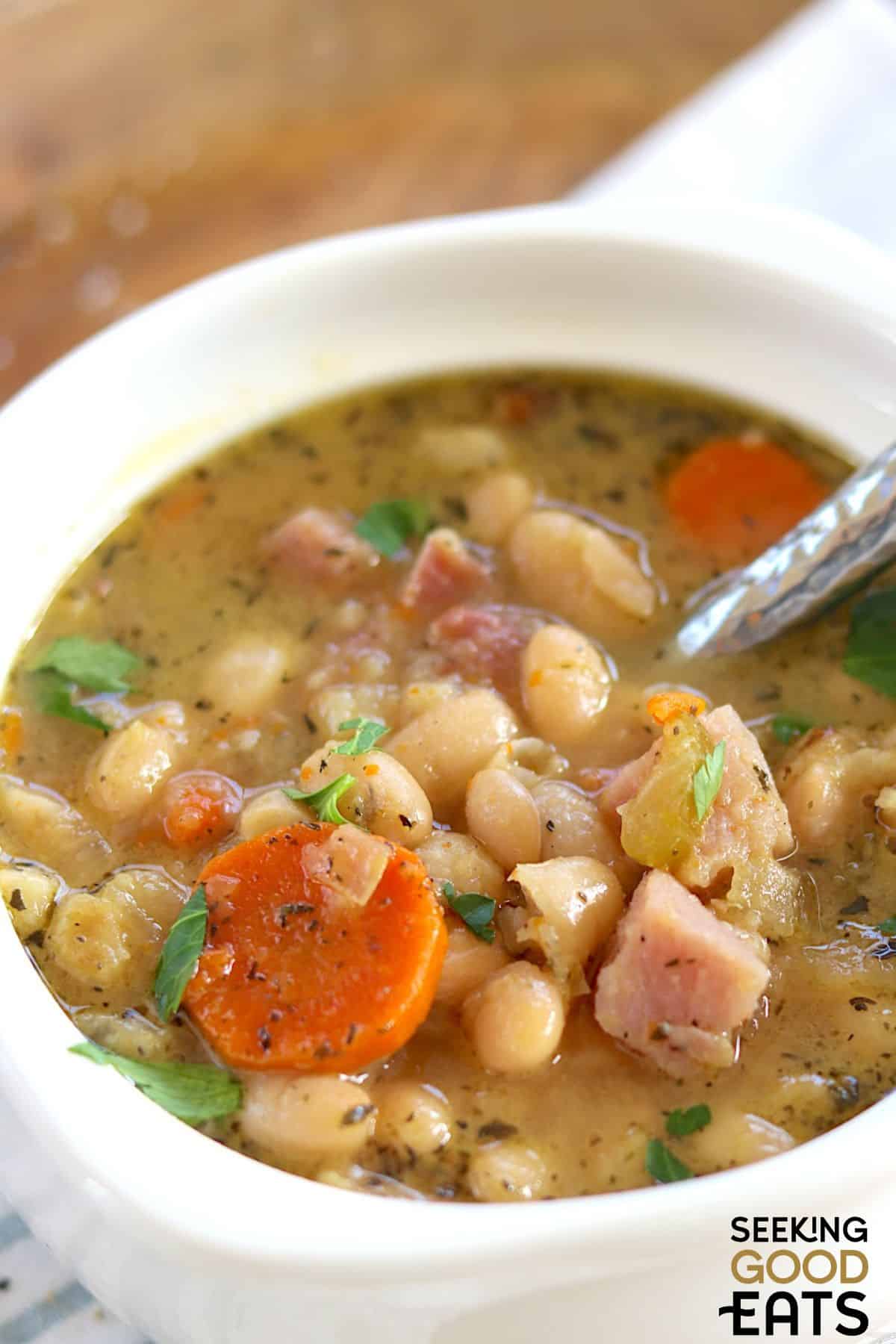 Ham and bean soup served in a white bowl with a spoon.