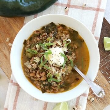 Chili with black eyed peans and collard greens in a white round bowl and silver spoon.