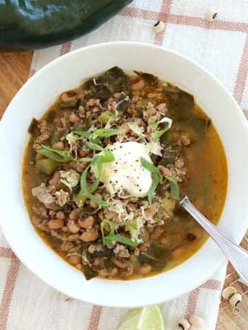 Chili with black eyed peans and collard greens in a white round bowl and silver spoon.