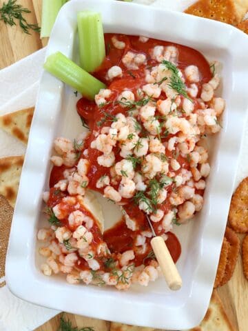 Cream cheese shrimp dip on a white dish with crackers and celery for dipping.