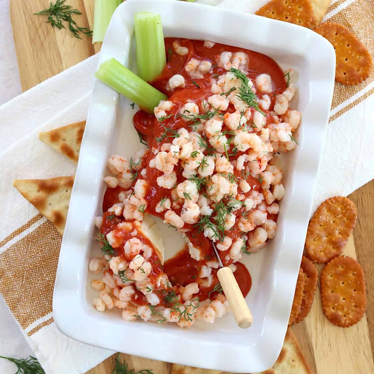 Cream cheese shrimp dip on a white dish with crackers and celery for dipping.