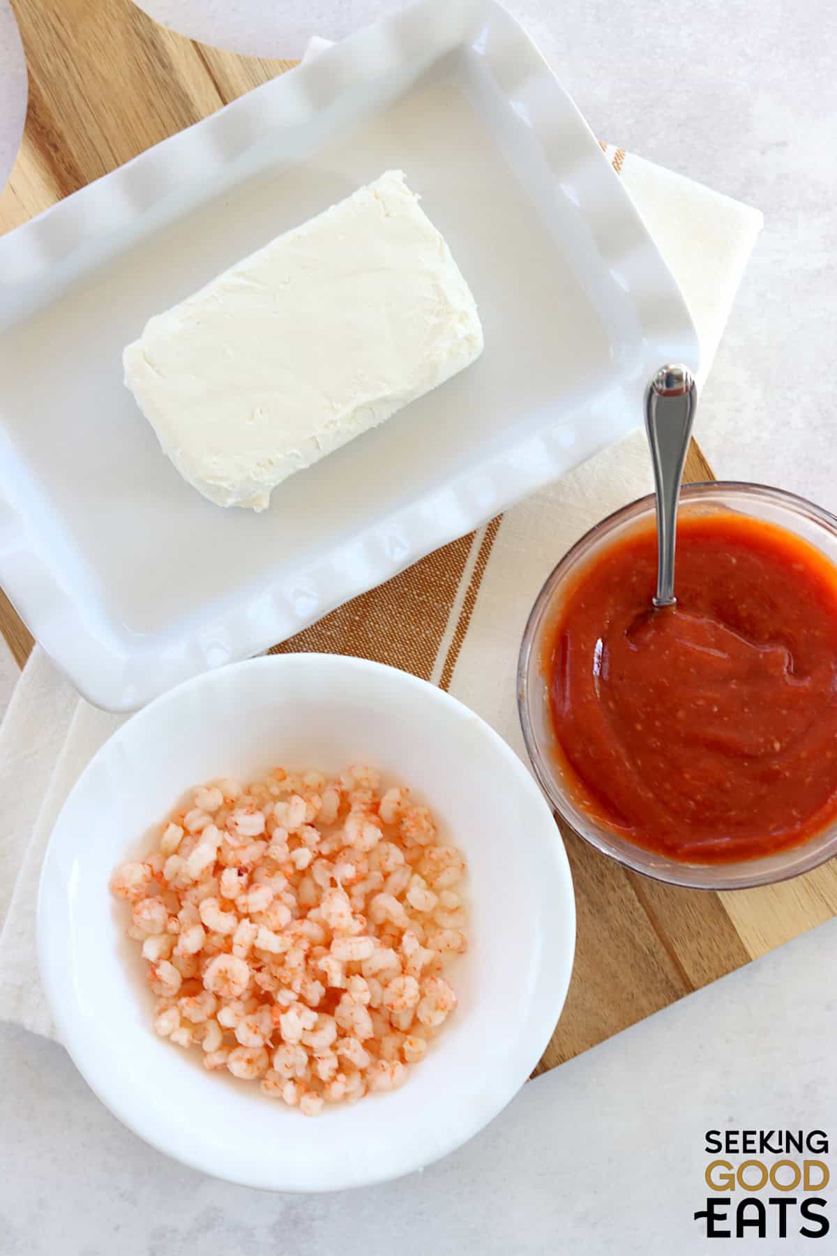 Ingredients needed for making shrimp dip with cream cheese on a white board.