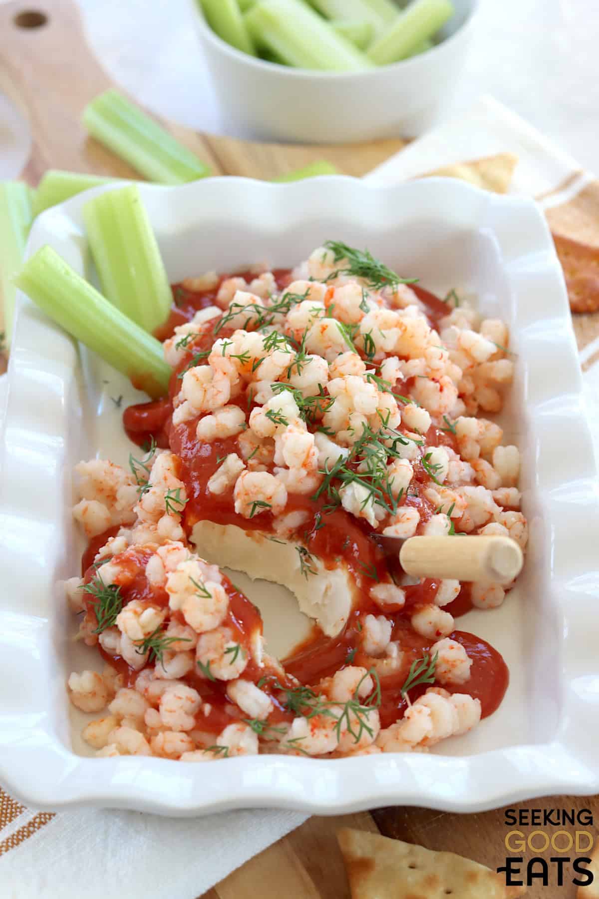 A white serving dish with cream cheese shrimp dip topped with fresh dill.
