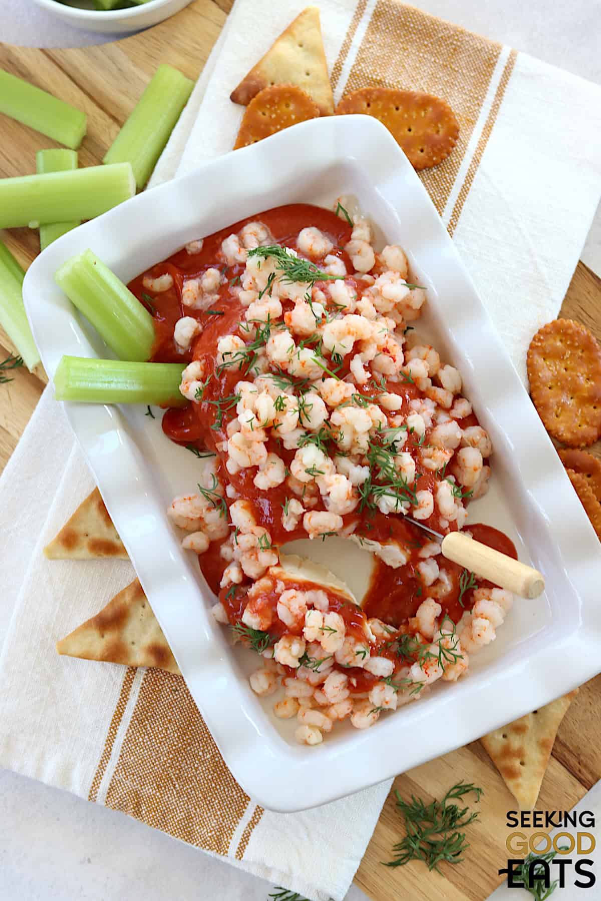 Cream cheese shrimp dip in a white rectangle dish with crackers and celery.