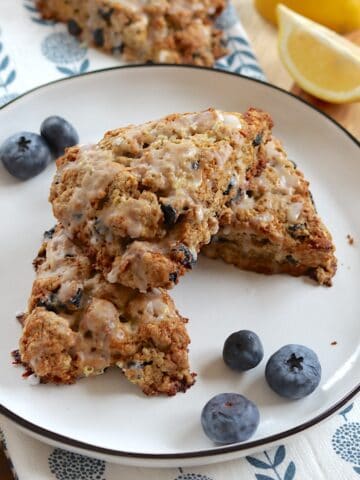 Vegan lemon blueberry scones stack in three on a white round plate.
