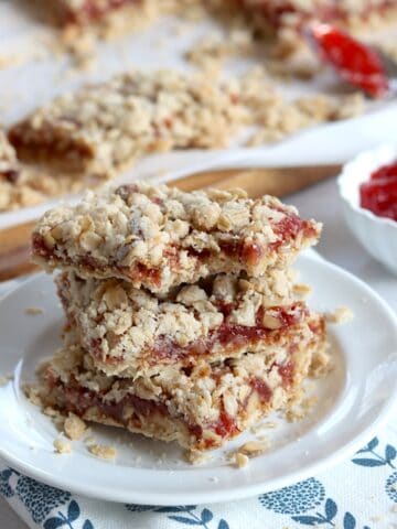 Three strawberry oatmeal bars stacked on a small white plate.