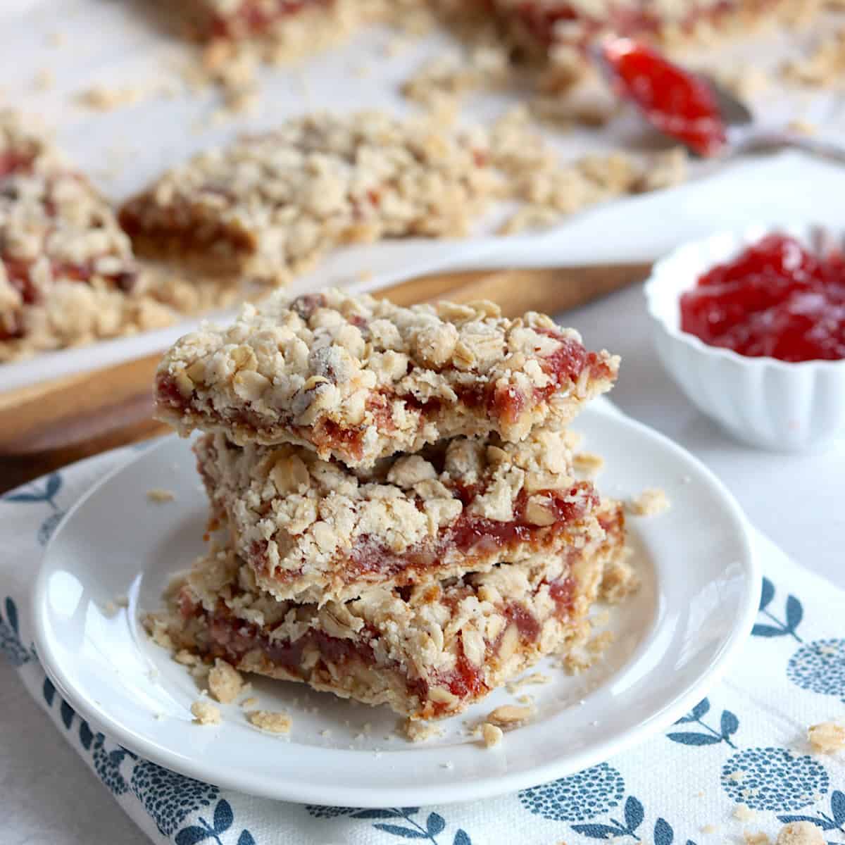 Three strawberry oatmeal bars stacked on a small white plate.