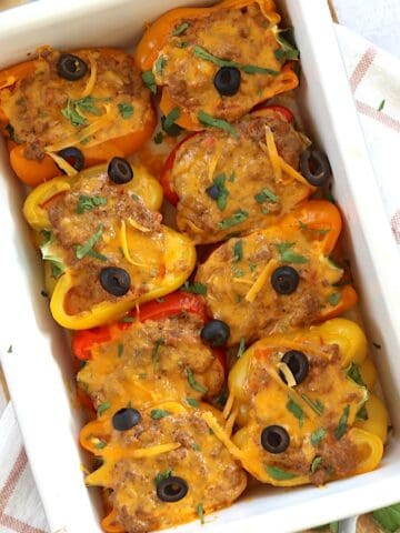 A white baking dish of stuffed taco peppers with melted cheese and olives on top.