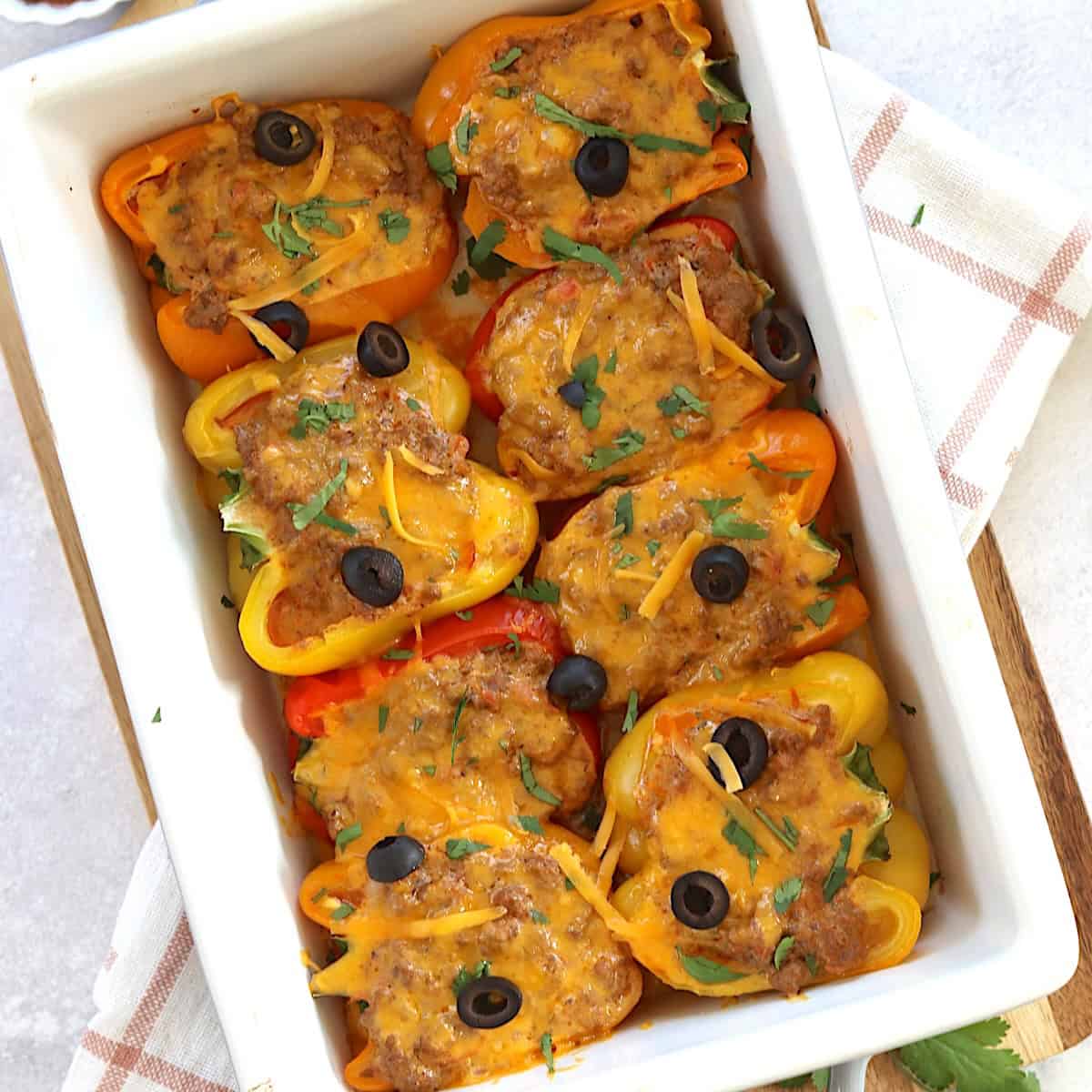 A white baking dish of stuffed taco peppers with melted cheese and olives on top.