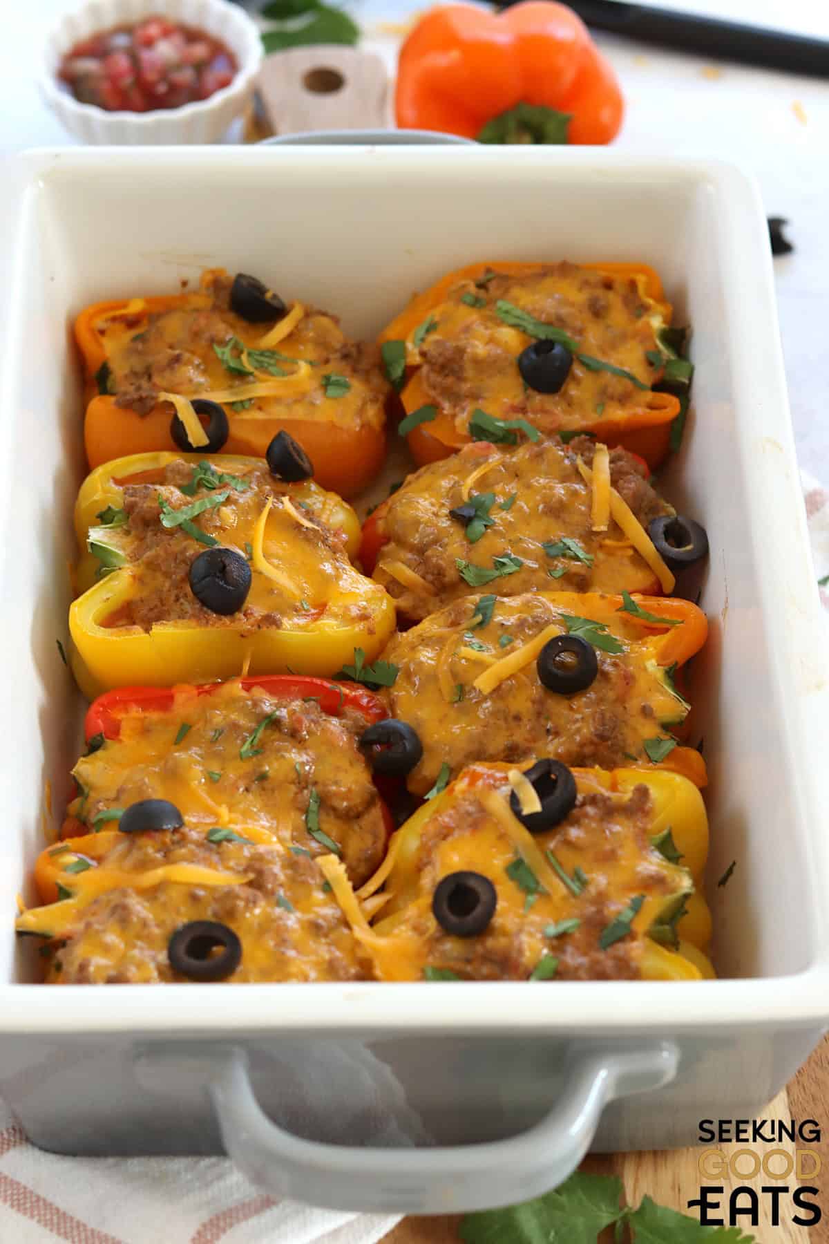A gray and white casserole dish of baked stuffed taco peppers with olives on top.