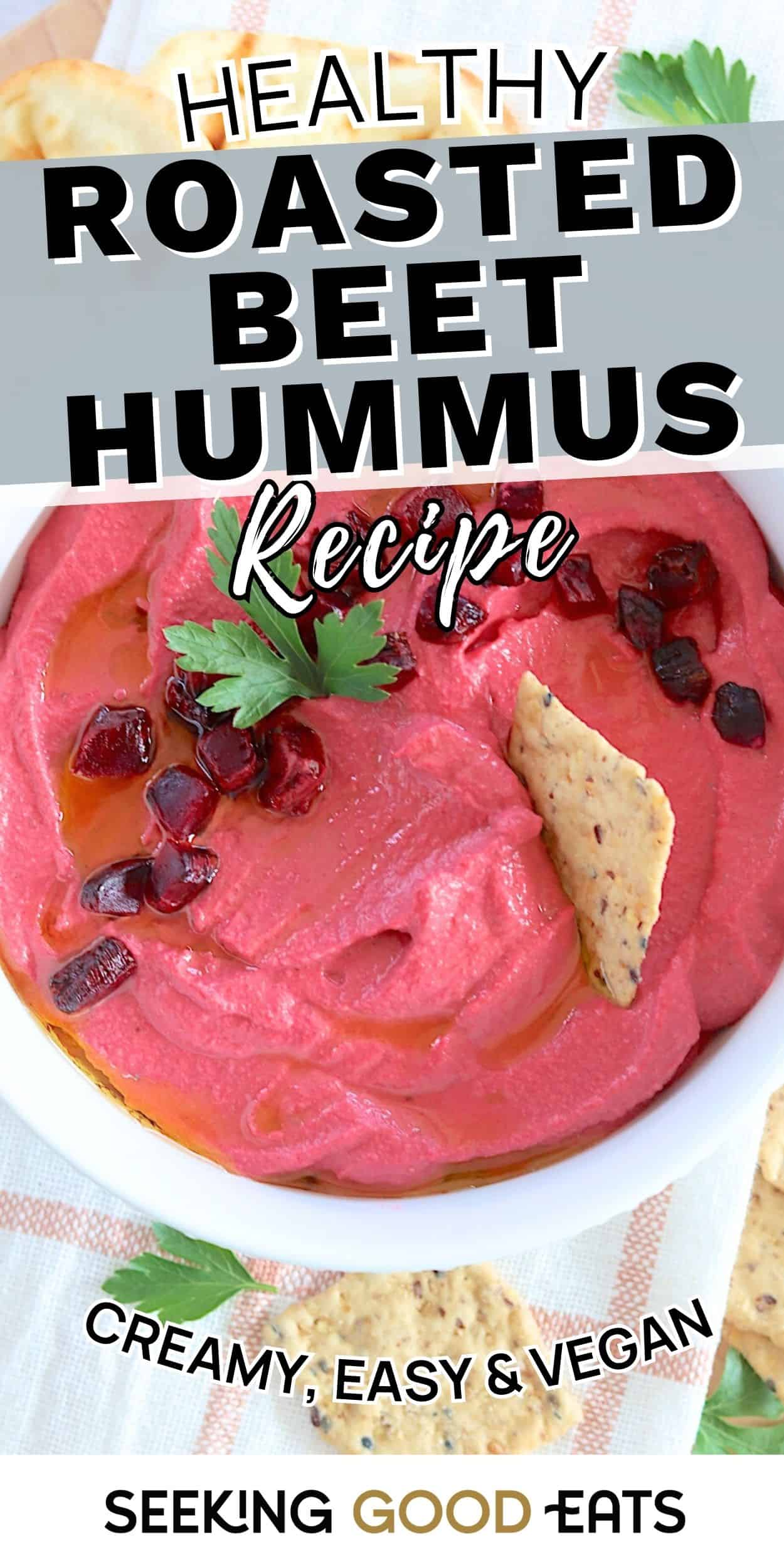 A bowl of bright pink roasted beet hummus topped with parsley and diced beets, served with crackers. This creamy vegan hummus recipe is shown as a colorful appetizer.
