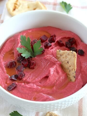 Roasted beet hummus served in a white round bowl and garnished with diced beets and crackers.