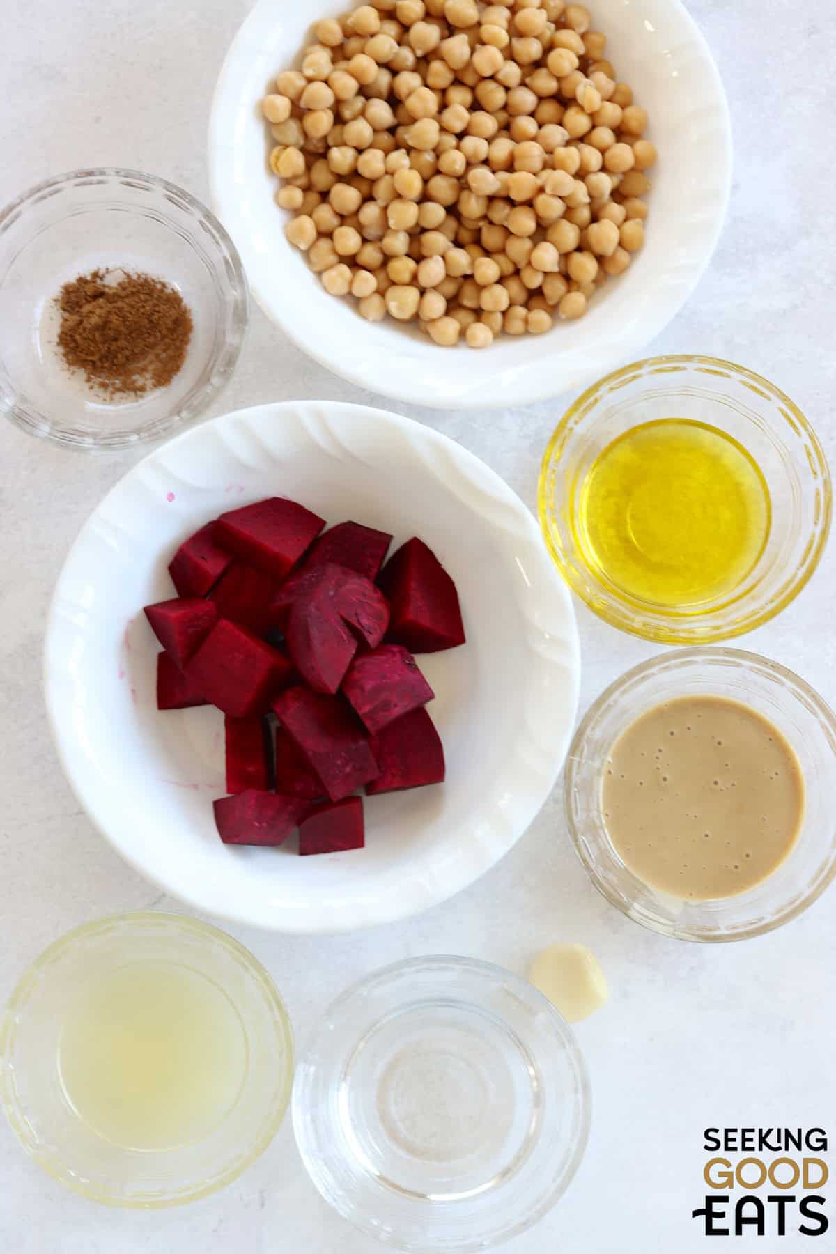 Ingredients needed to make roasted beet hummus arranged on a white marble countertop.