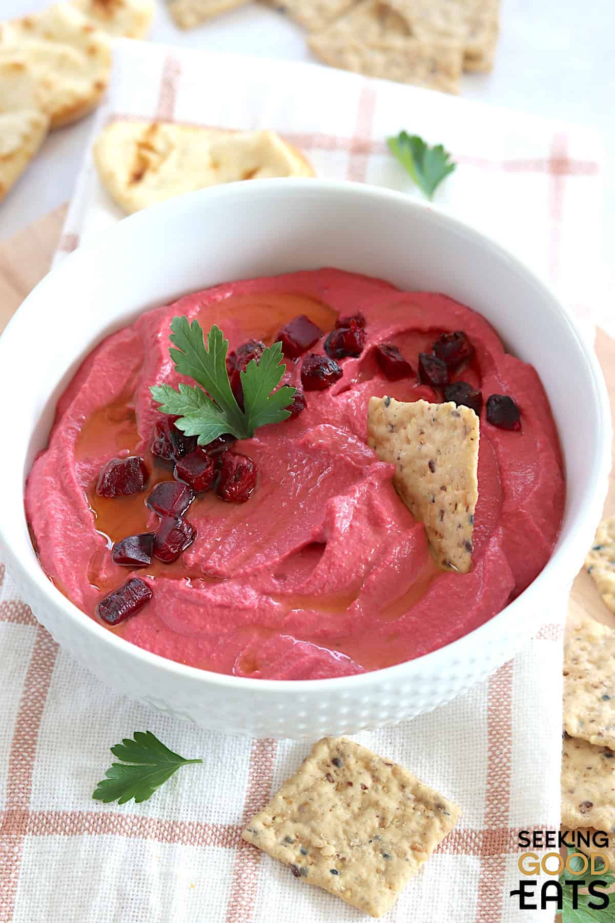 Roasted beet hummus served in a white round bowl and garnished with diced beets and crackers.