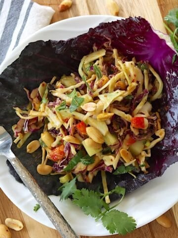 A white plate with Thai salad with cabbage and peanuts.