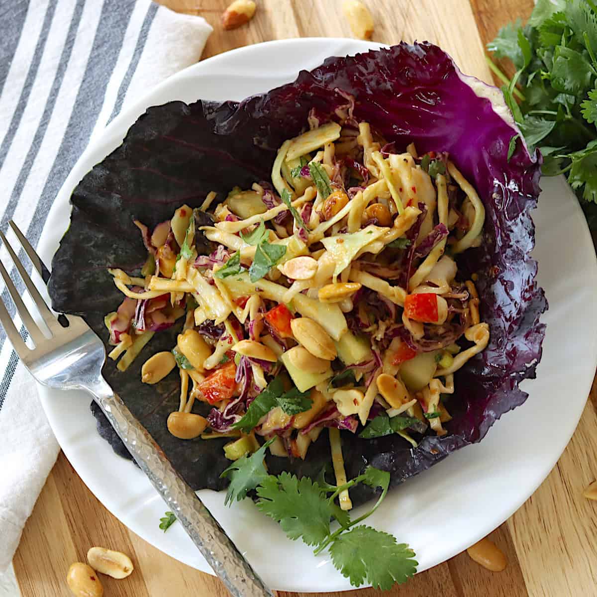 A white plate with Thai salad with cabbage and peanuts.