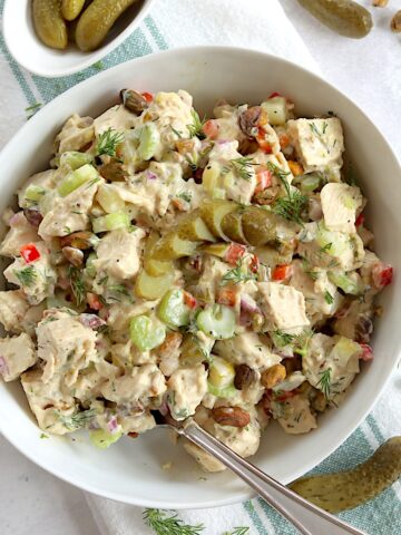 Dill pickle chicken salad served in a white bowl and a silver spoon garnished with fresh dill.