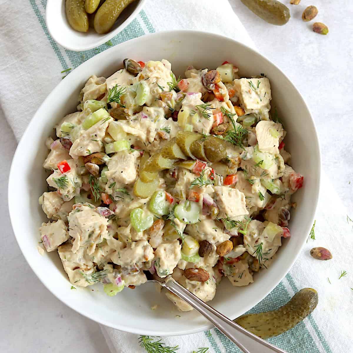 Dill pickle chicken salad served in a white bowl and a silver spoon garnished with fresh dill.