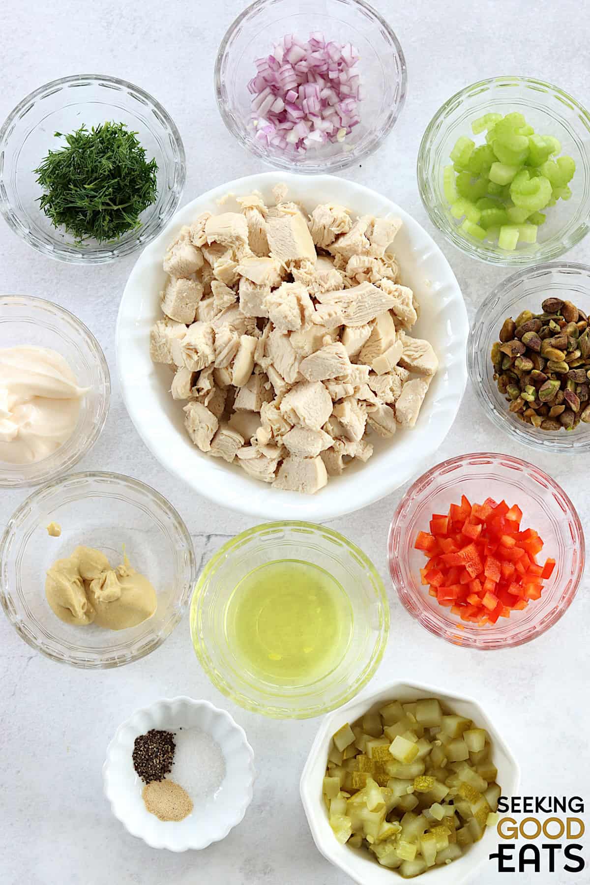Ingredients needed to make dill pickle chicken salad on a white marble countertop.