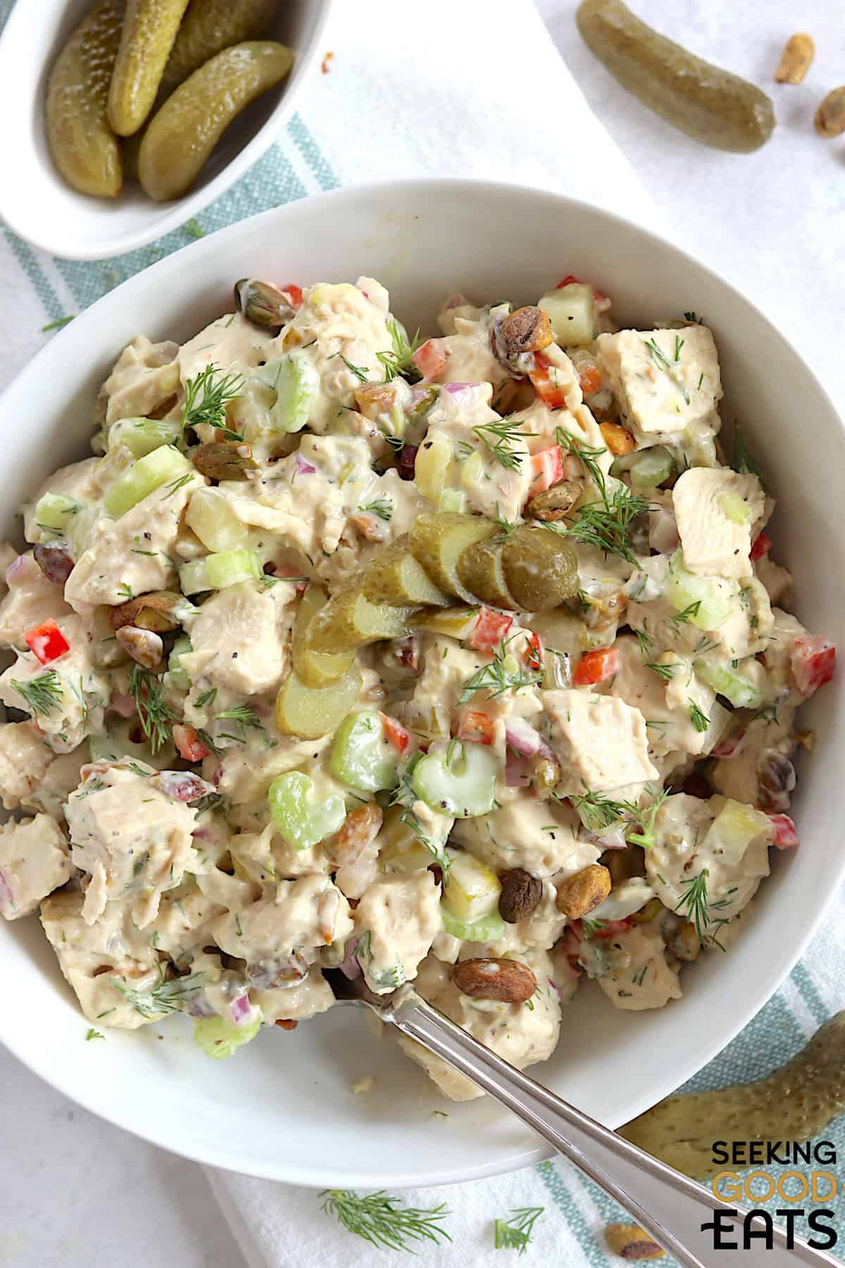 Dill pickle chicken salad served in a white bowl and a silver spoon garnished with fresh dill.