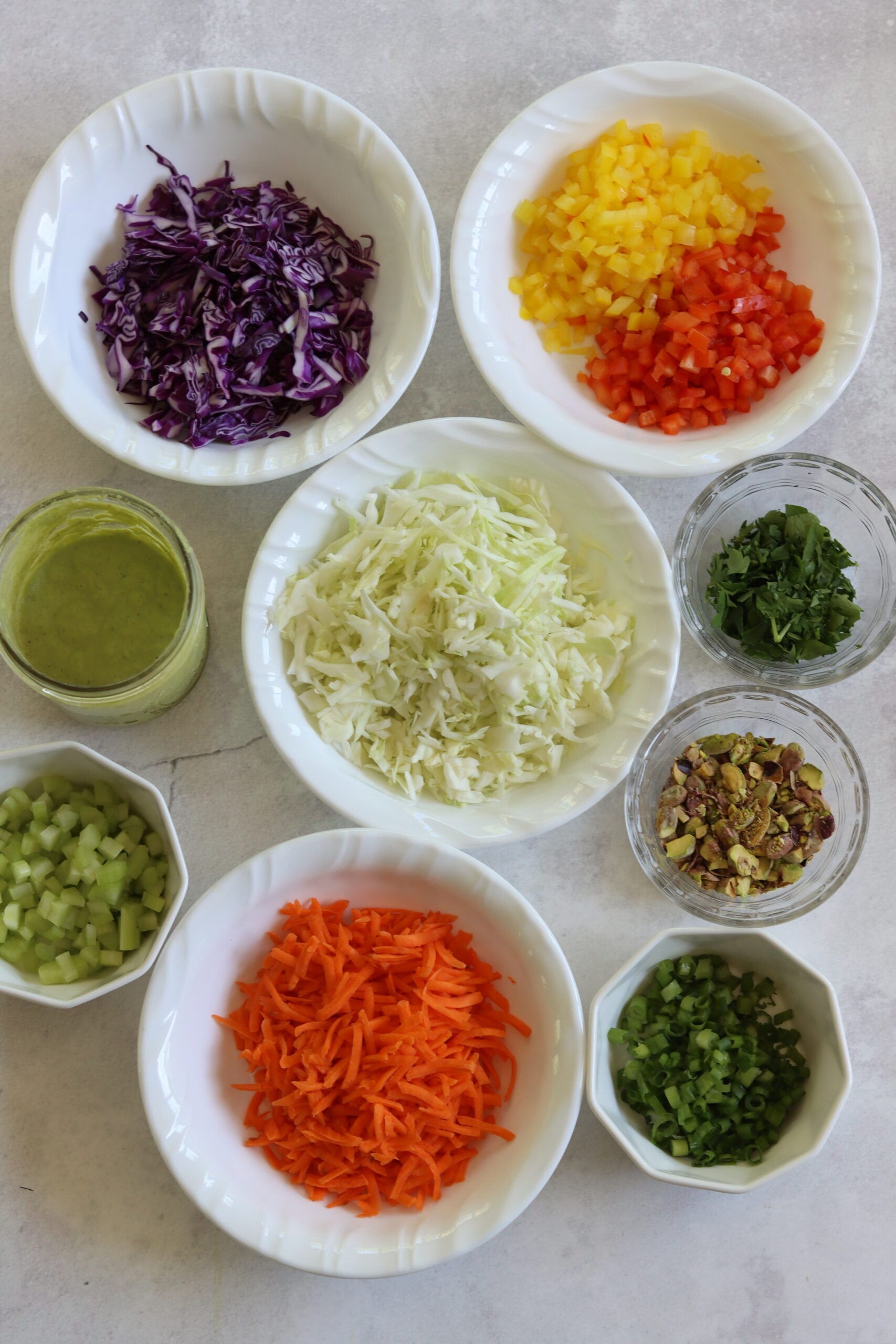 Ingredients needed to make green goddess cabbage salad arranged on a white marble countertop.