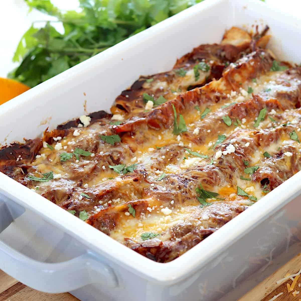 Steak enchiladas recipe in a gray baking dish with cilantro.