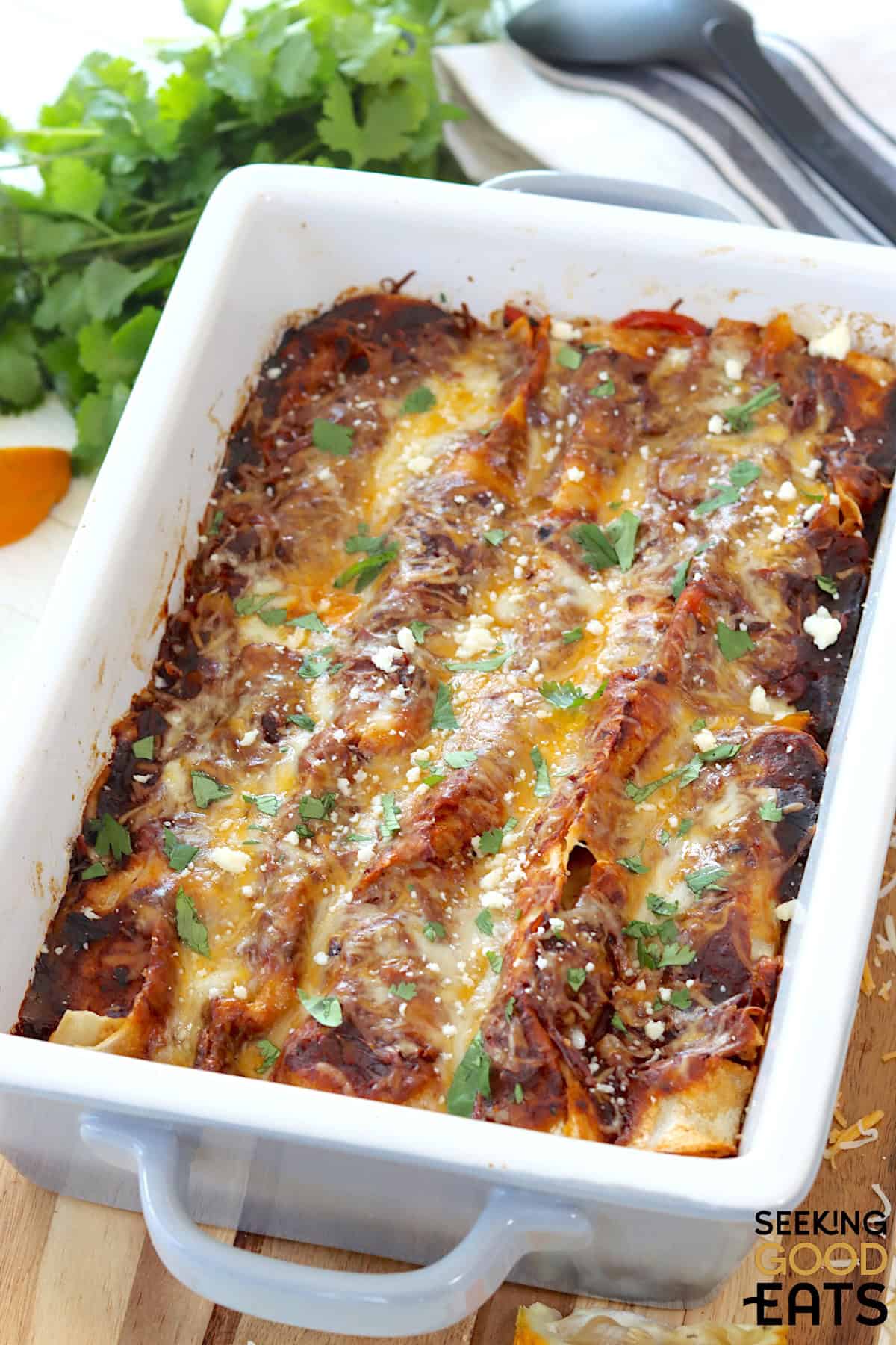 A gray and white baking dish of beef enchiladas with red sauce