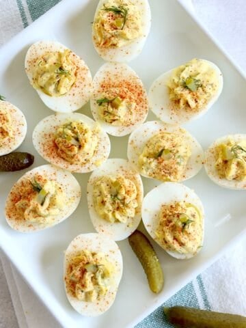 Dill pickle deviled eggs on a square white plate garnished with diced dill pickle and fresh dill.