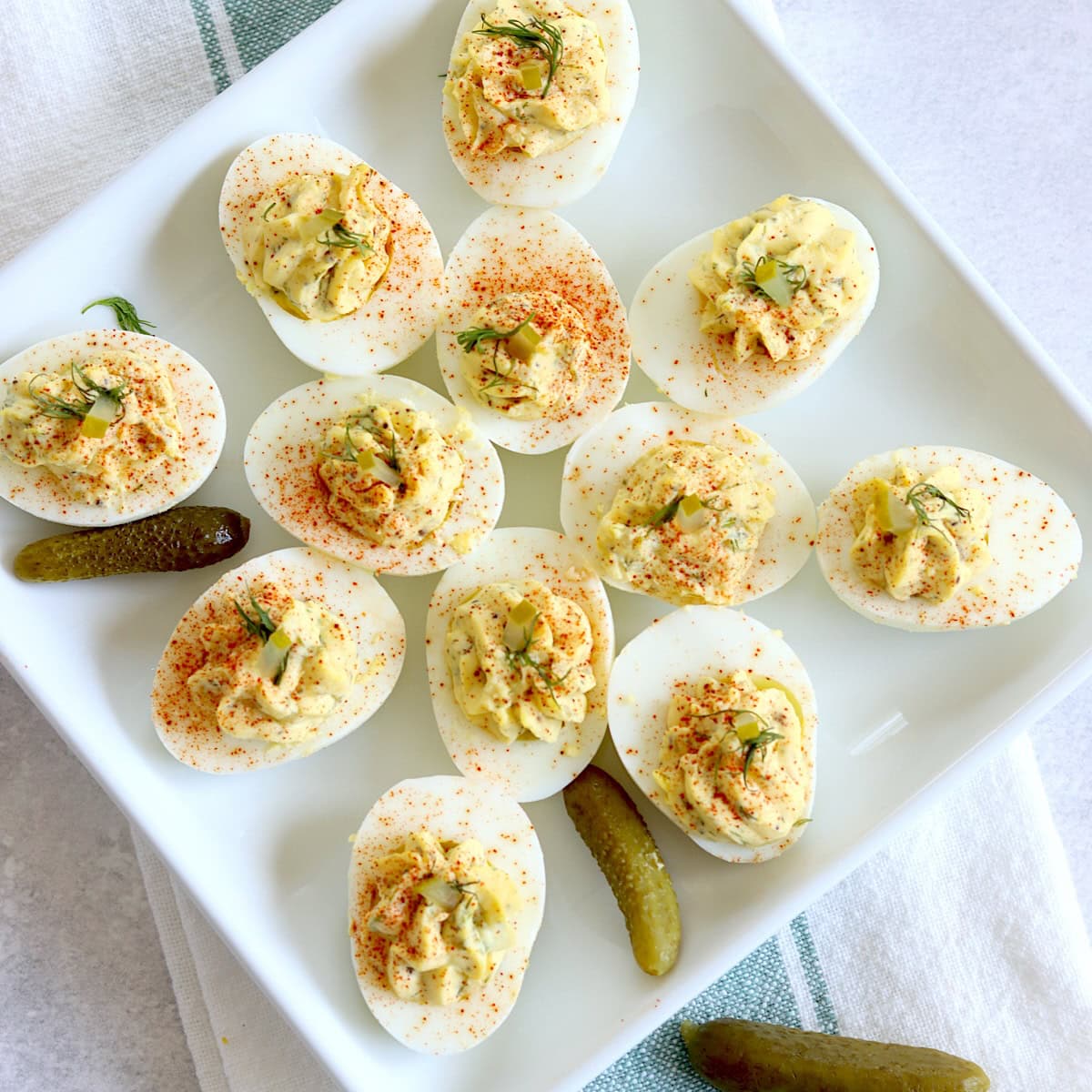 Dill pickle deviled eggs on a square white plate garnished with diced dill pickle and fresh dill.