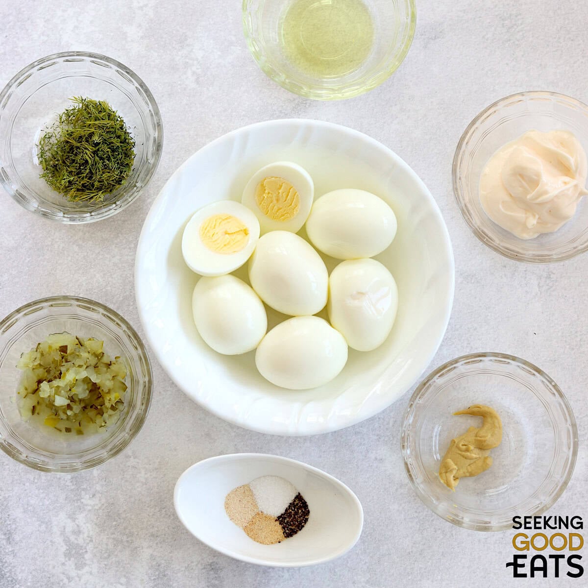 Ingredients needed to make dill pickle deviled eggs on a white marbled countertop.