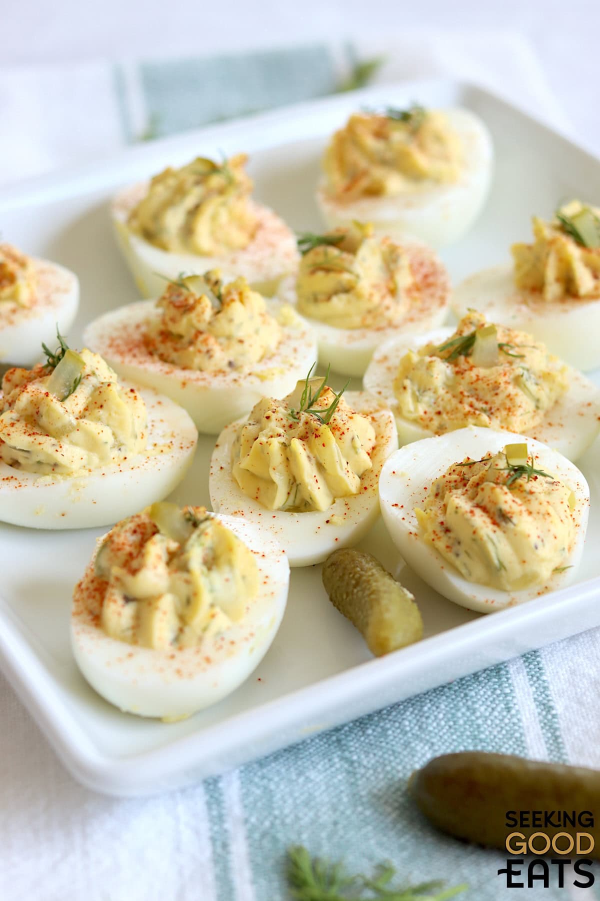 Dill pickle deviled eggs on a square white plate garnished with diced dill pickle and fresh dill.