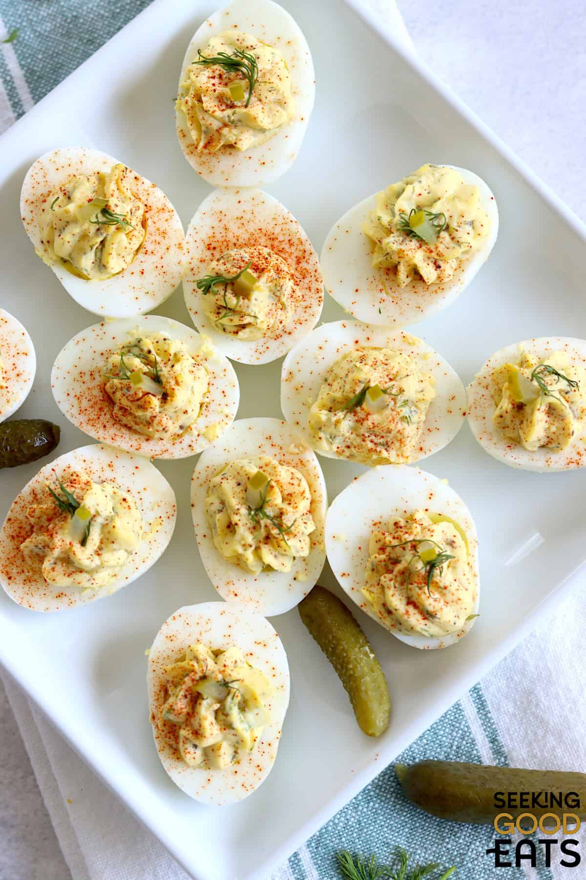 Dill pickle deviled eggs on a square white plate garnished with diced dill pickle and fresh dill.