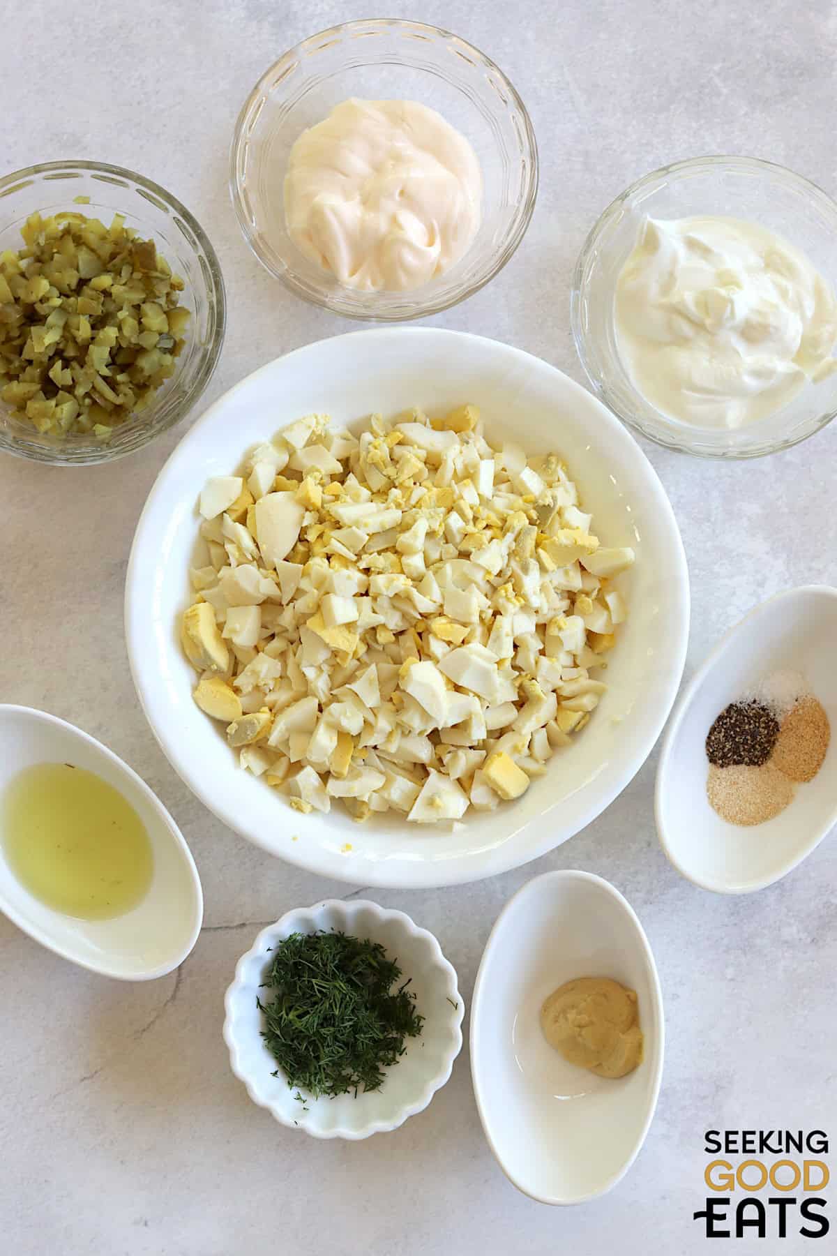 Ingredients needed to make egg salad with dill pickles on a white marble countertop.