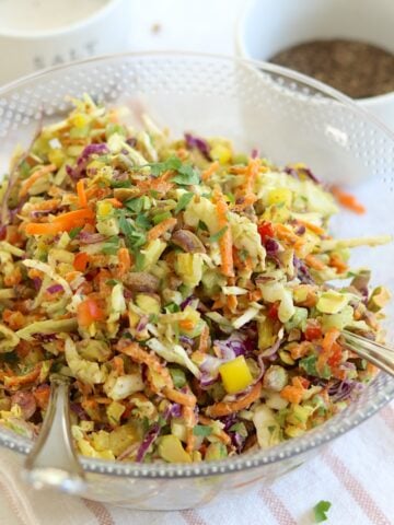 Green goddess cabbage salad served in a clear bowl and two silver serving spoons.