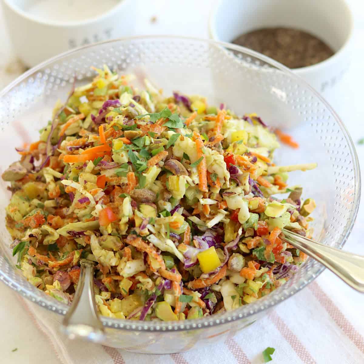 Green goddess cabbage salad served in a clear bowl and two silver serving spoons.