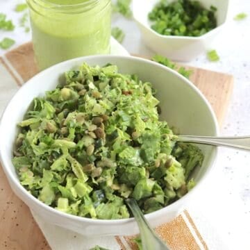 Green goddess salad recipe in a round white bowl and two silver salad forks.