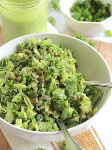 Green goddess salad recipe in a round white bowl and two silver salad forks.