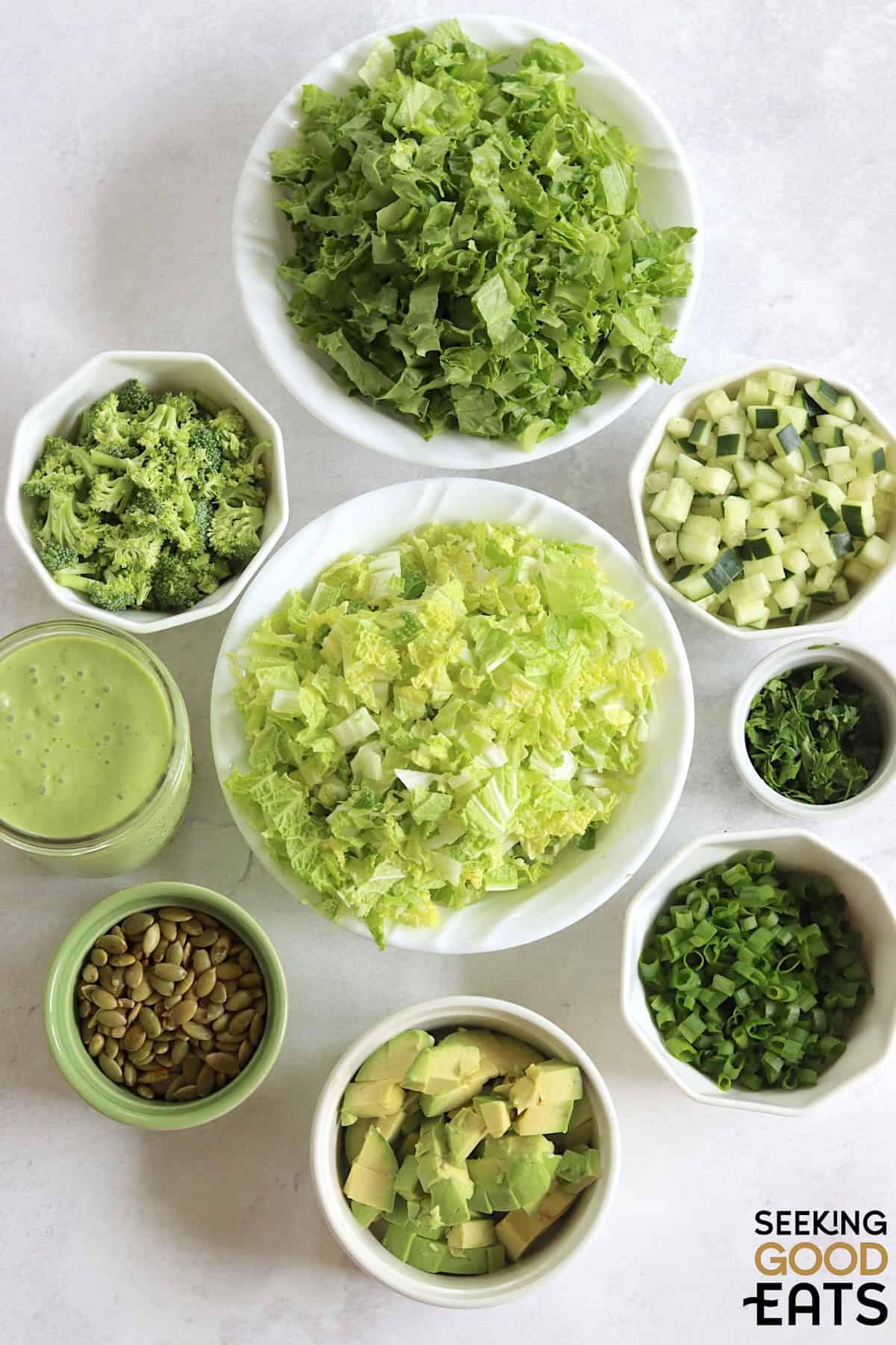 Ingredients needed to make green goddess salad recipe on a white marble countertop.
