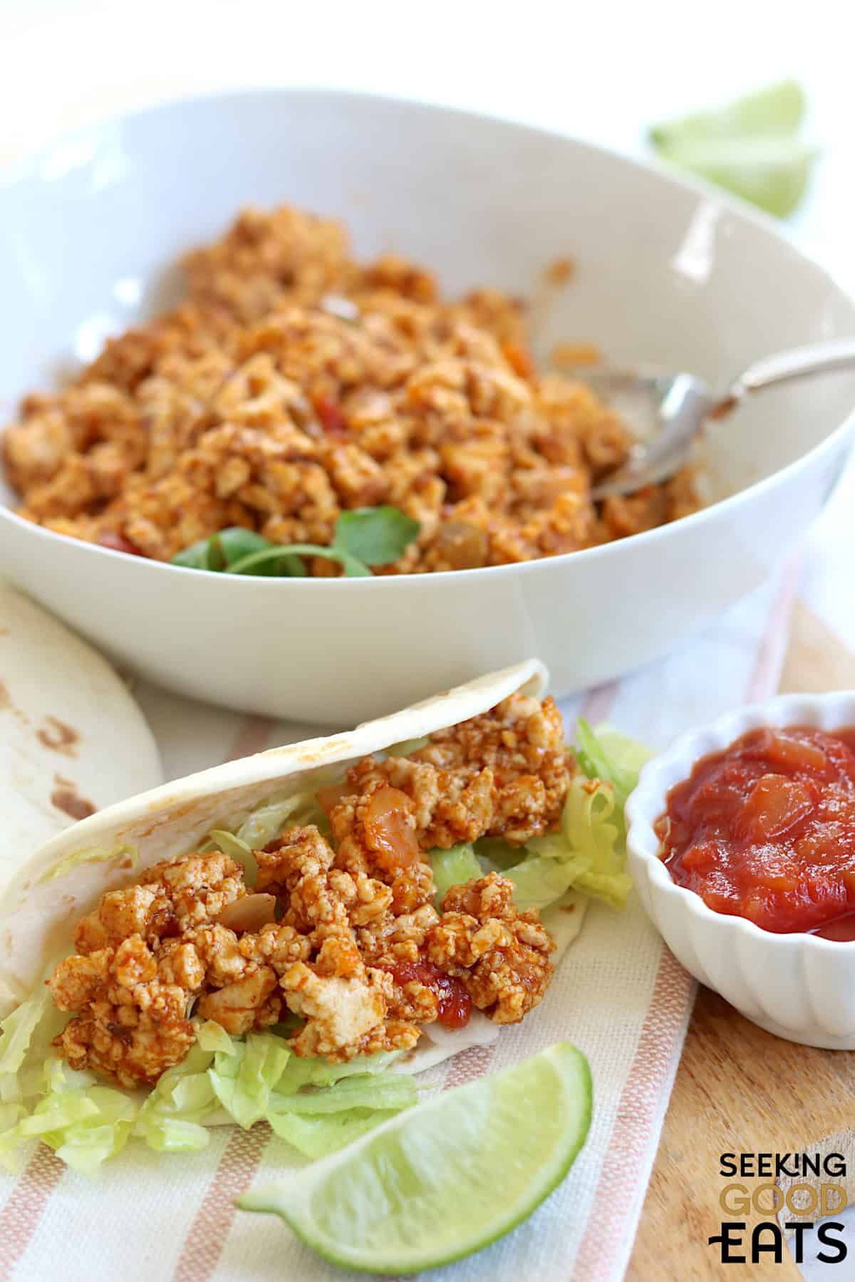 Plant based tofu taco meat in a round white bowl and a silver serving spoon next to a soft shell taco.