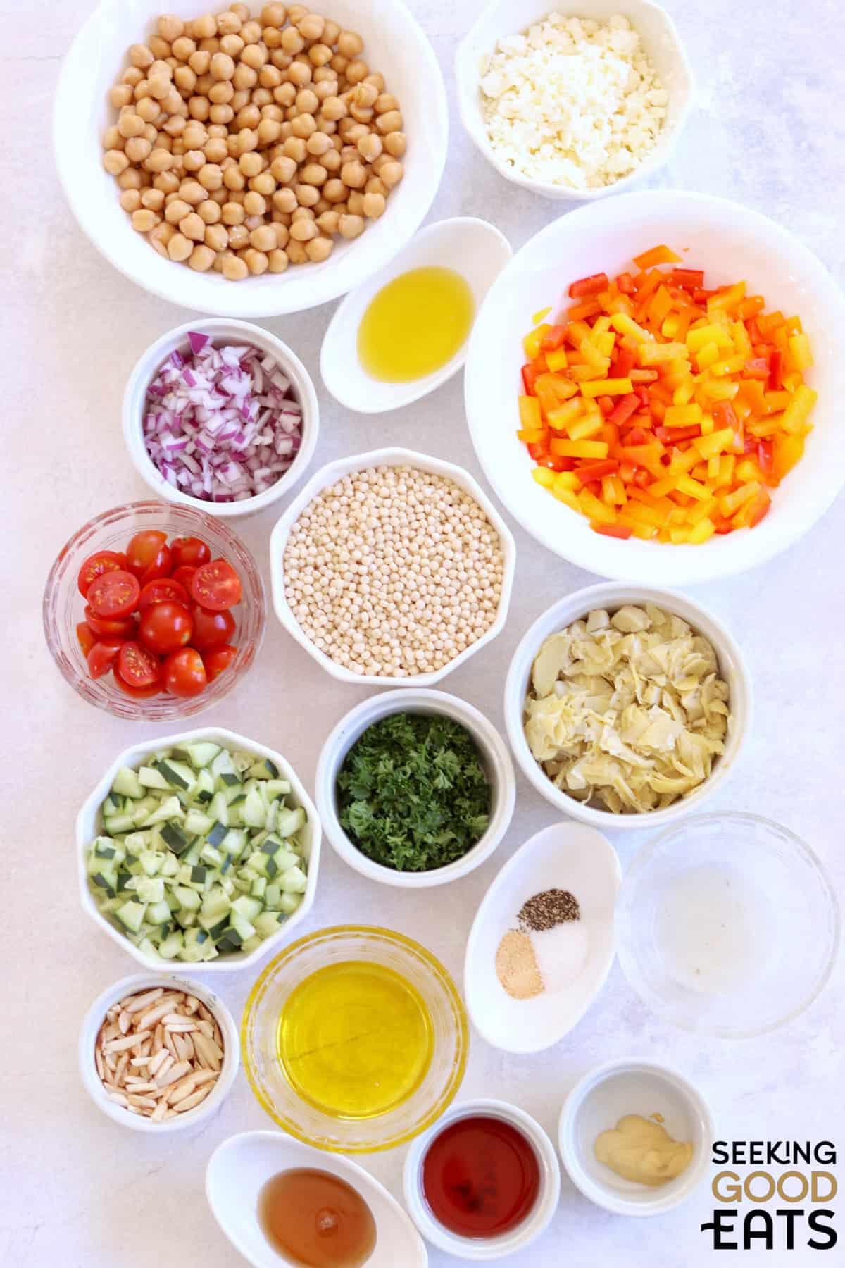 Ingredients needed to make Mediterranean pearl couscous salad on a white marble countertop.